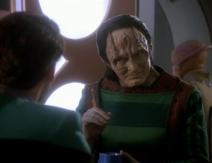 Seated over a meal in the replimat, Garak lifts as a finger while speaking with Dr. Bashir in 'Cardassians'