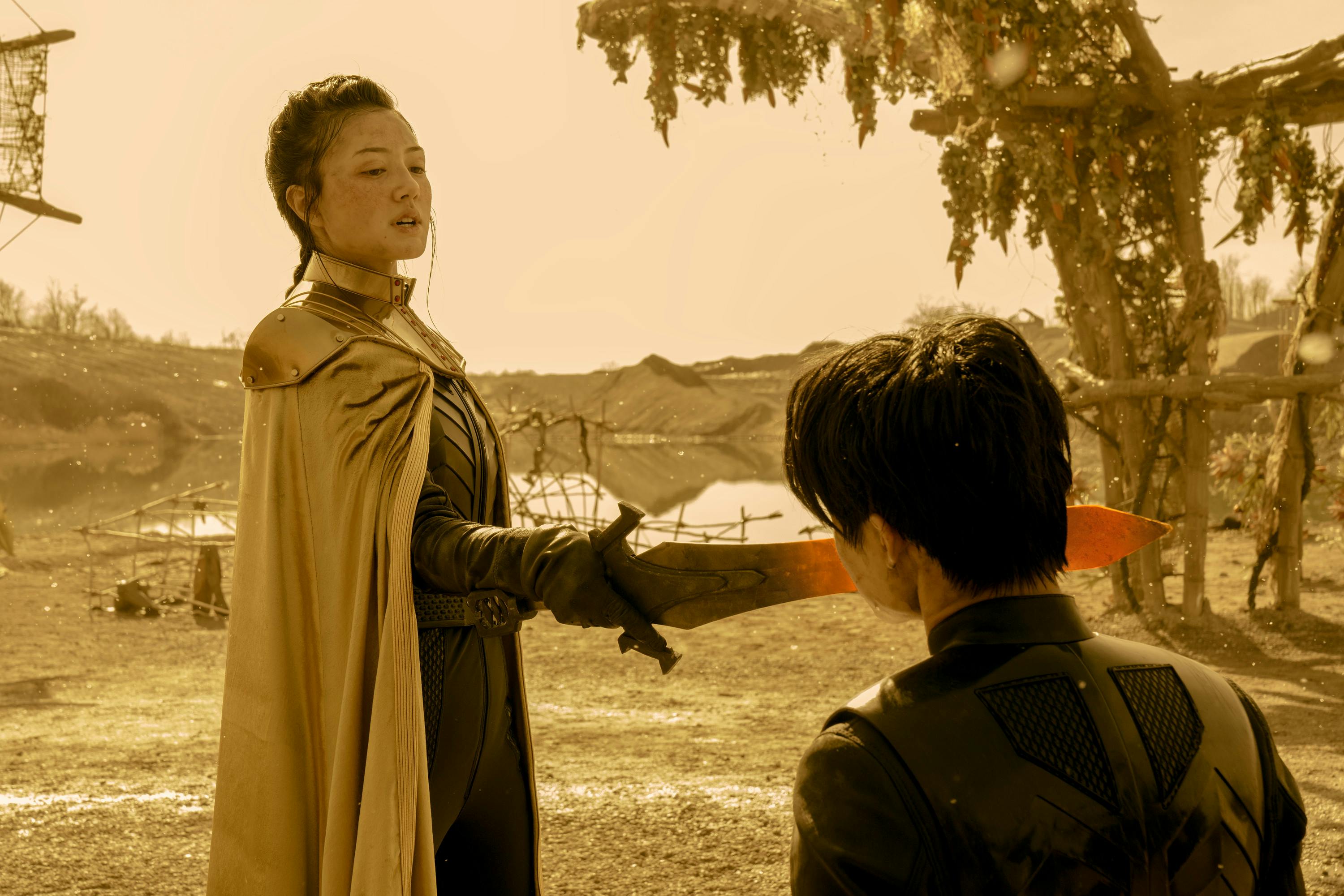 Young Philippa Georgiou, donning her yellow emperor's cloak, raises the heated blade of her sword to a kneeling San's face in Star Trek: Section 31