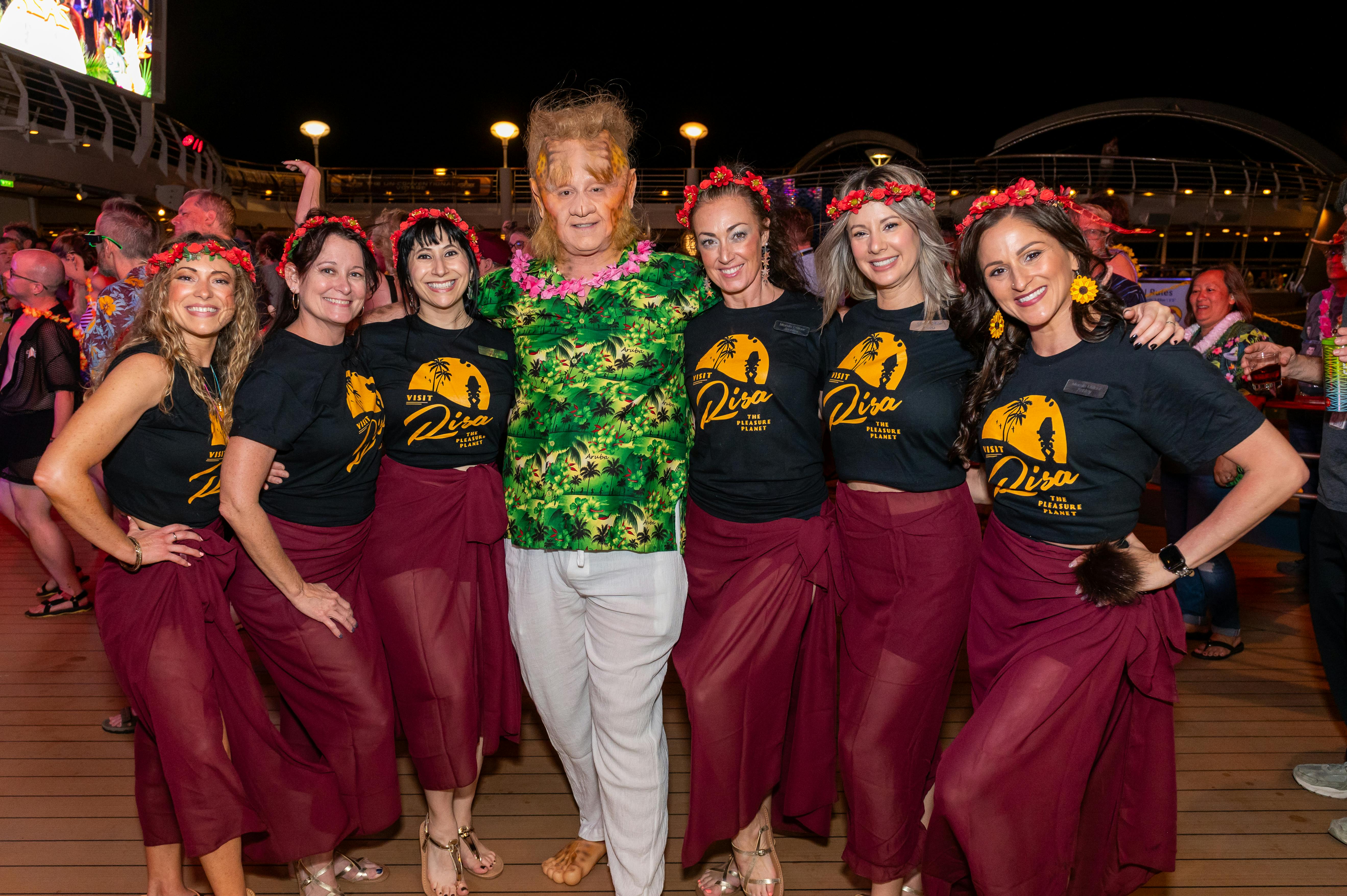 Aboard the pool deck of Star Trek: The Cruise, a Neelix cosplayer in a Hawaiian shirt poses with a group in Risa night t-shirts