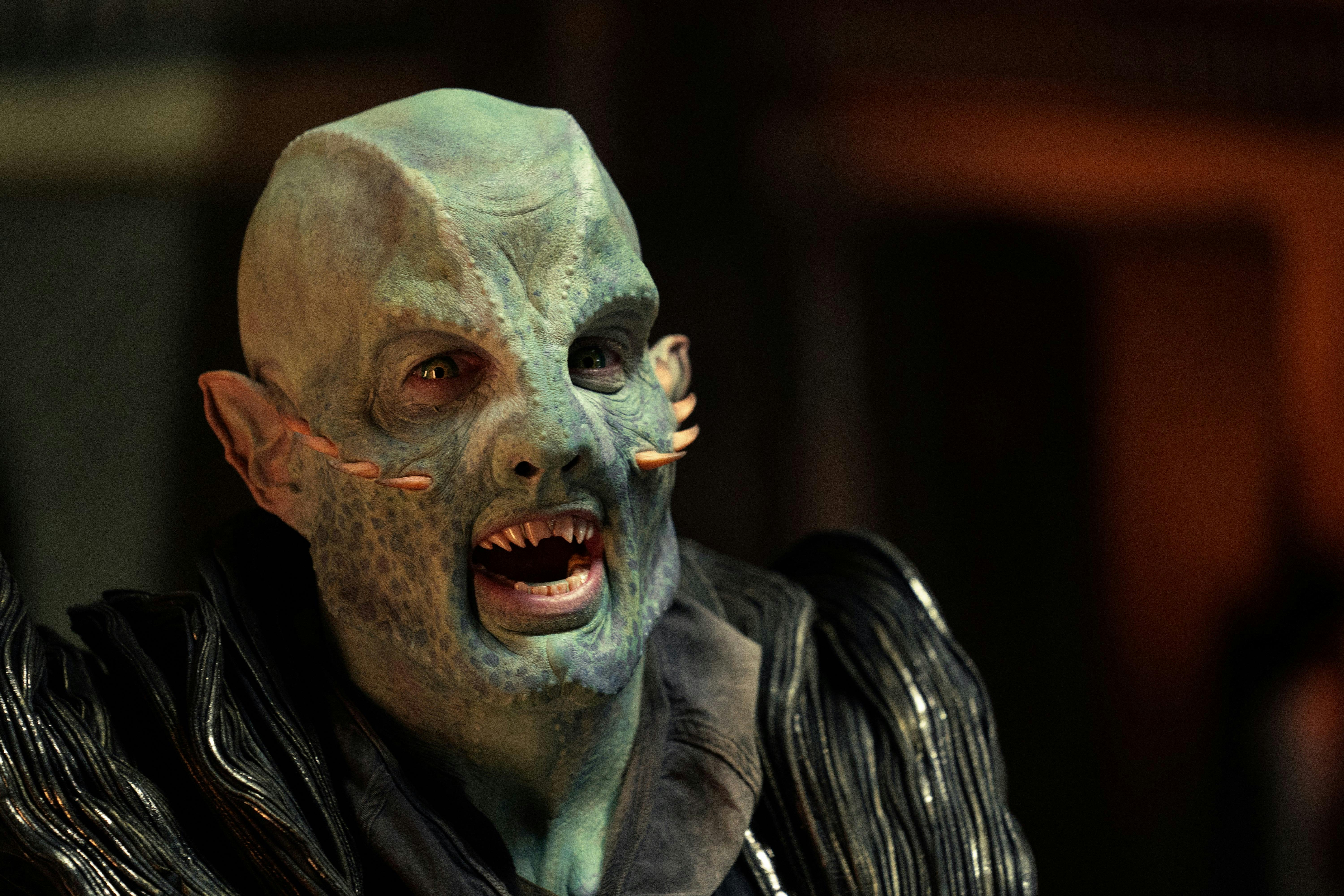 A blue-green alien with spikes on his face snarls at someone off camera.