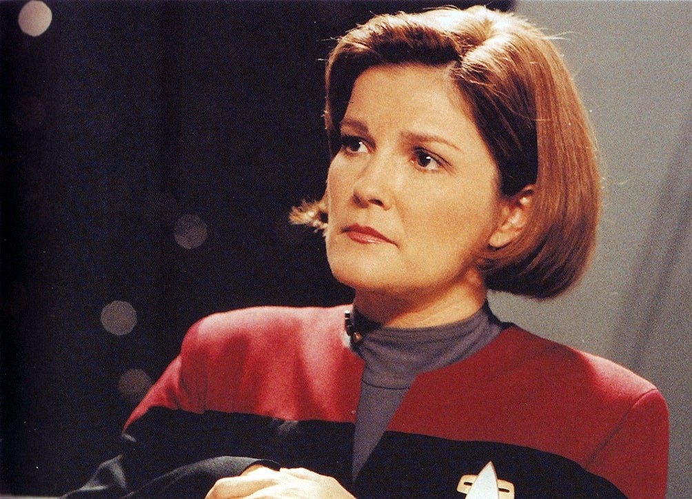 Captain Janeway glances over with a pensive gaze