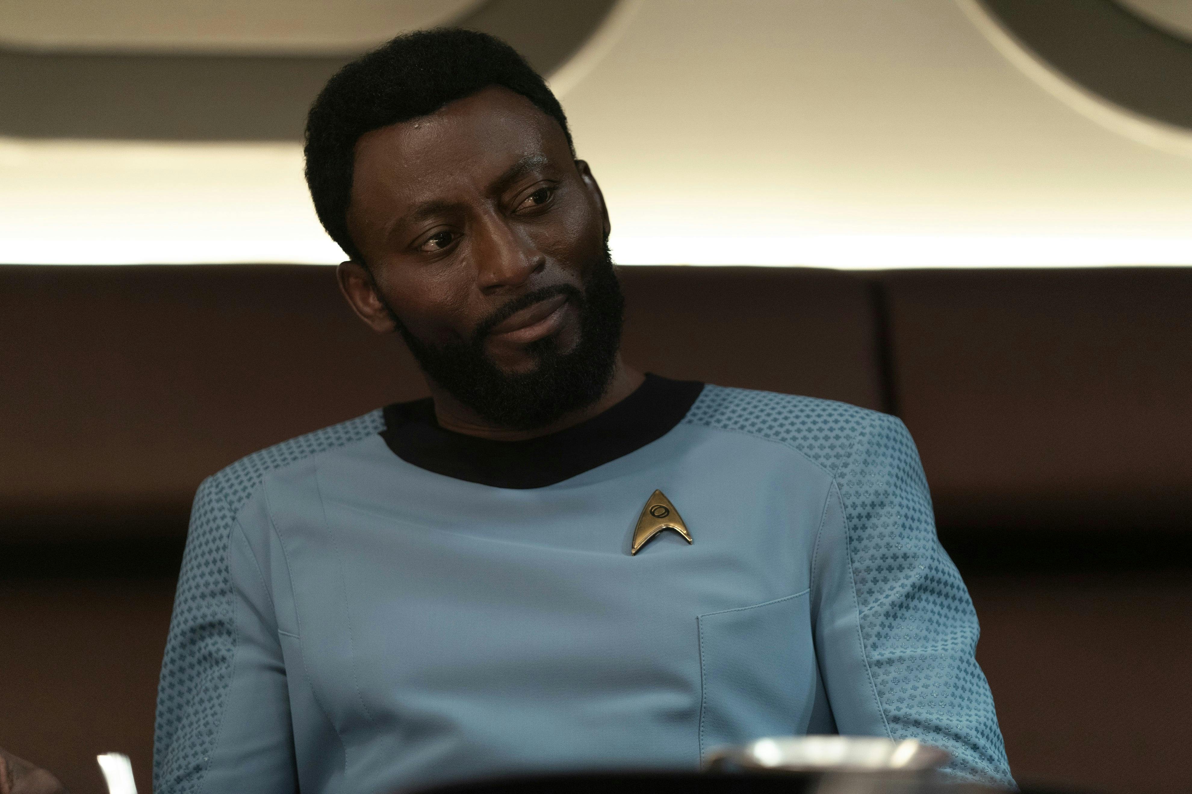 Close-up of Dr. M'Benga, sitting at the dinner table, at the captain's quarters and looking over at Dak'Rah with disdain in 'Under the Cloak of War'