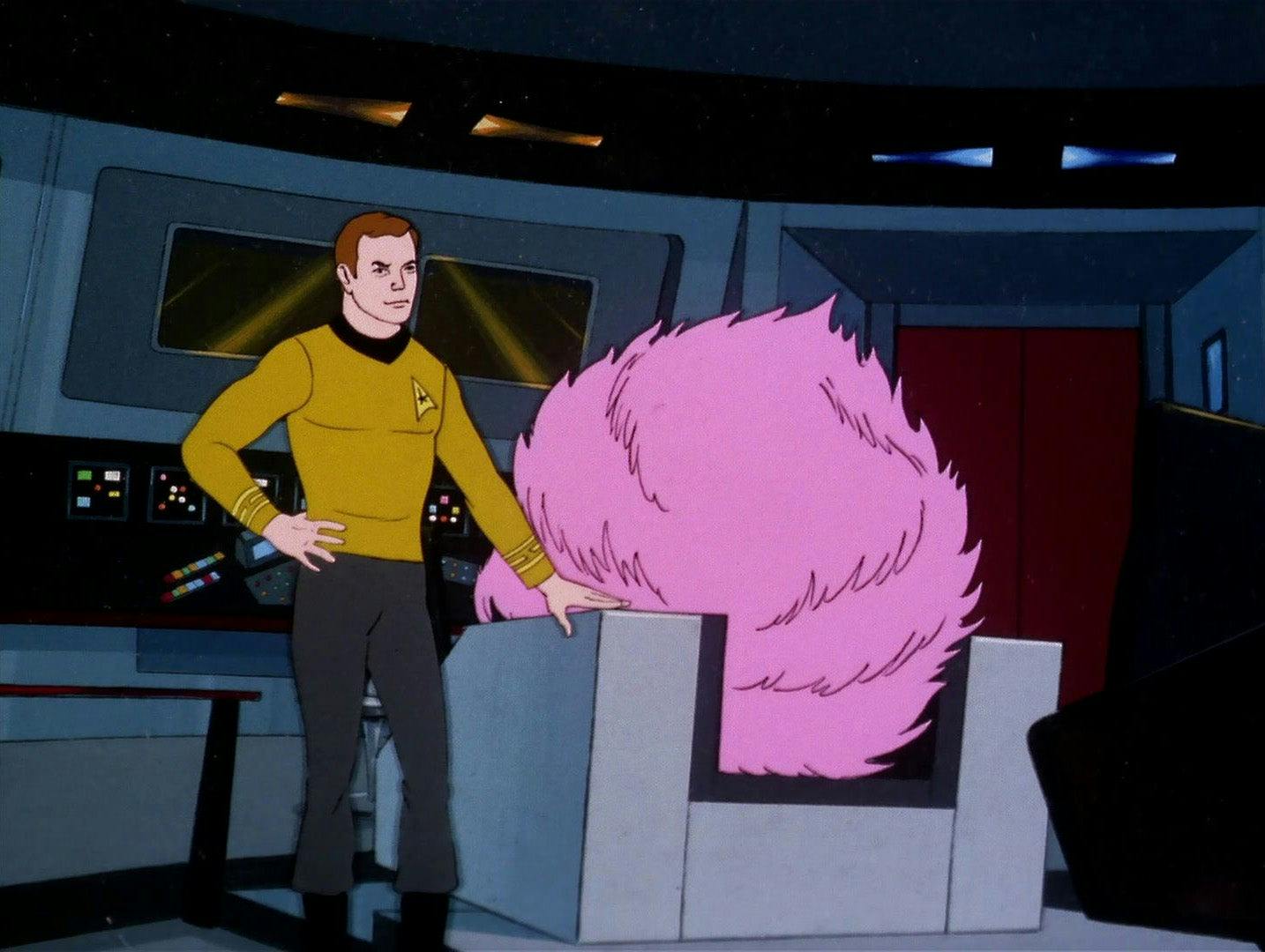 Captain Kirk stands next to a giant tribble perched in the captain's chair.