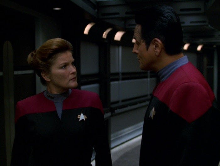 Janeway and Chakotay talk in a hallway.