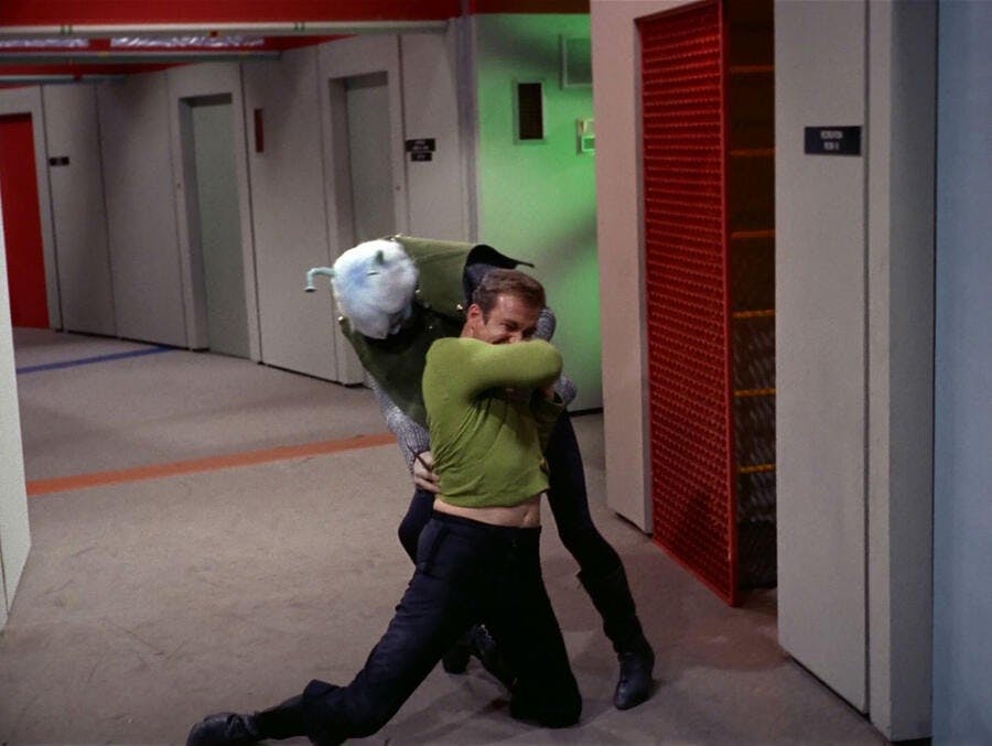 In a corridor, an Andorian has Kirk in a headlock and on his knees in 'Journey to Babel'