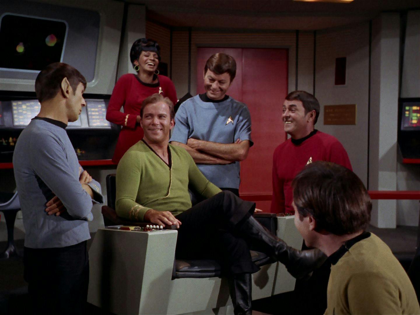 The Enterprise crew surround Kirk in the captain's chair in smiles and good spirits on Star Trek: The Original Series