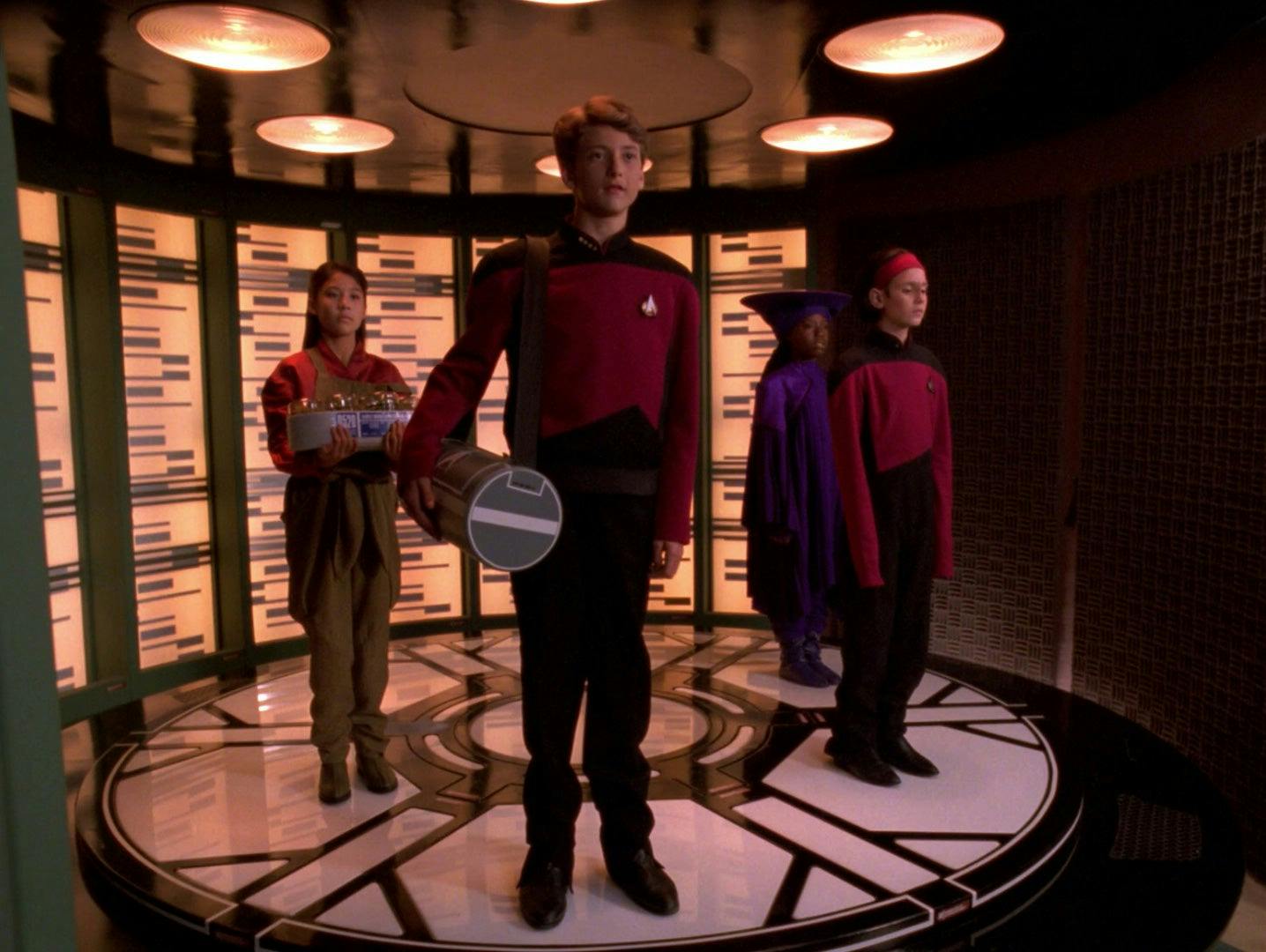 Twelve year old versions of Keiko, Picard, Ro Laren, and Guinan stand on the transporter pad in 'Rascals'