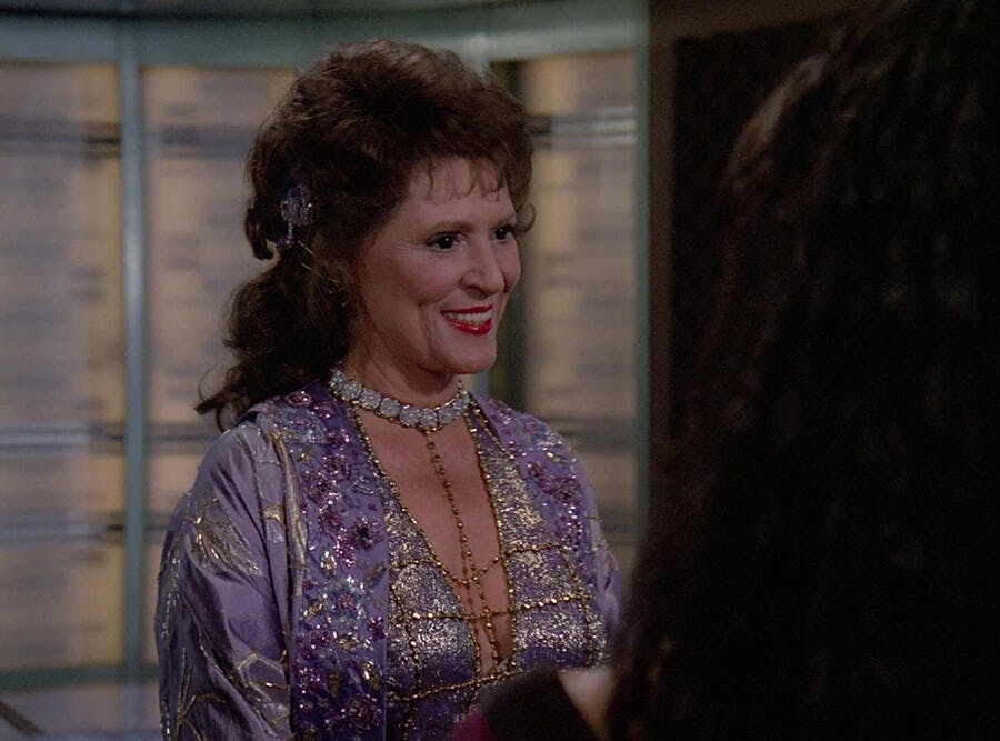 Ambassador Lwaxana Troi in front of the Enterprise-D's transporter pad in 'Manhunt'