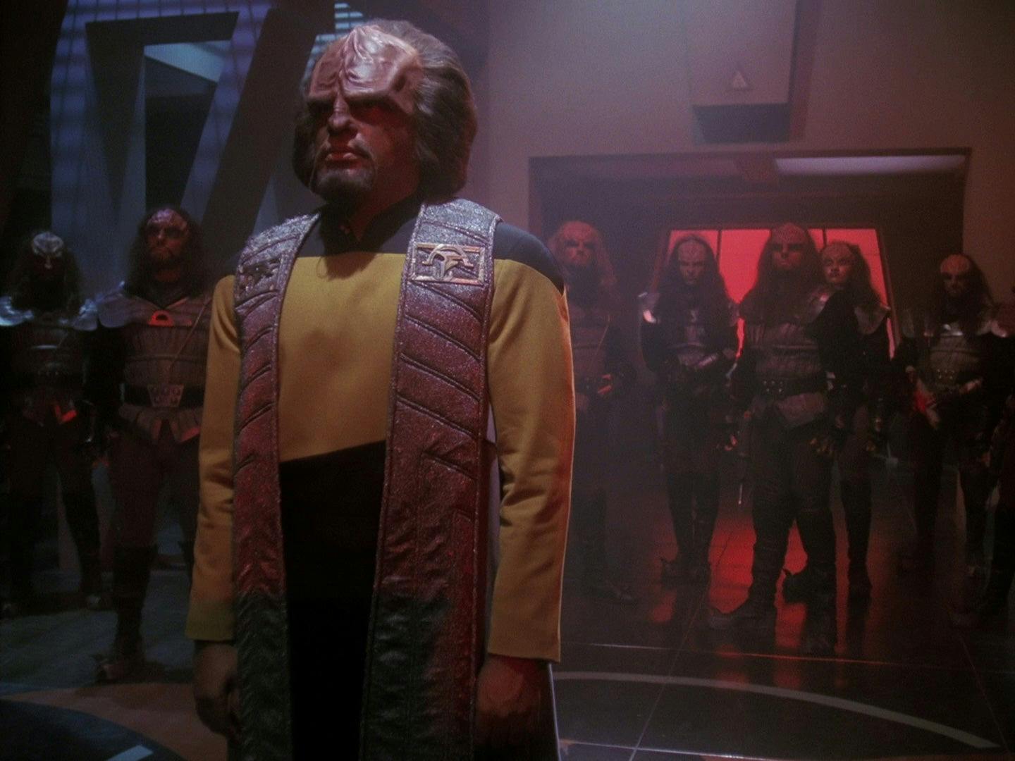 Worf stands before the Klingon High Council in his Starfleet uniform and ceremonial sash in 'Sins of the Father'