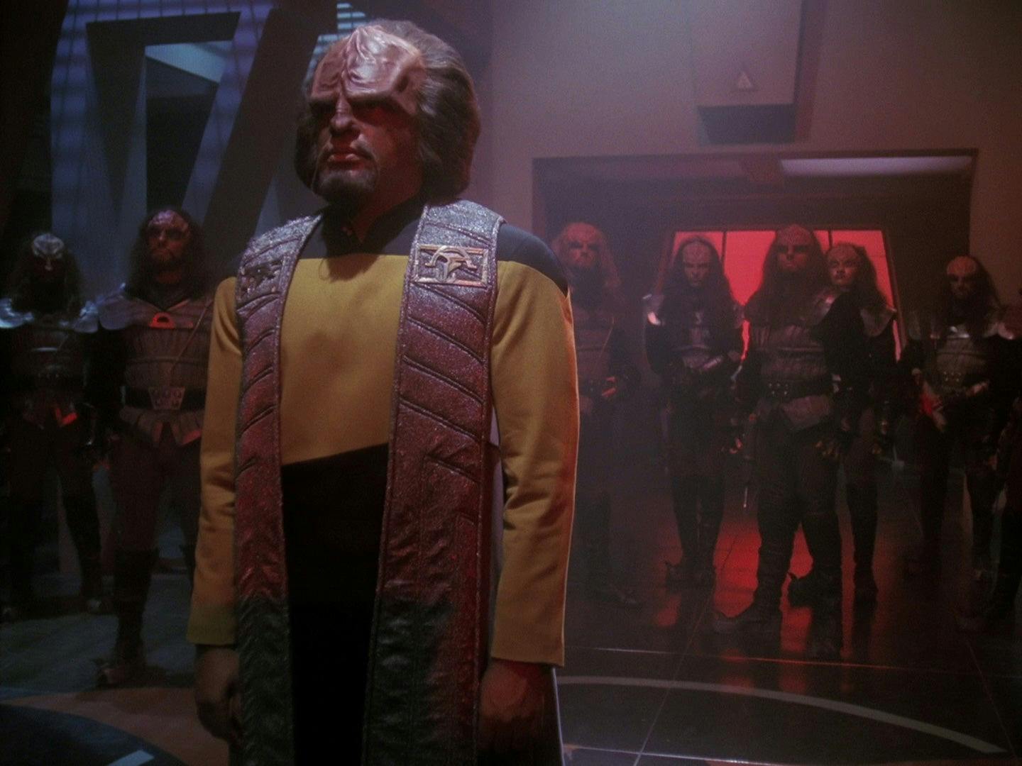 Worf stands in a darkened room.