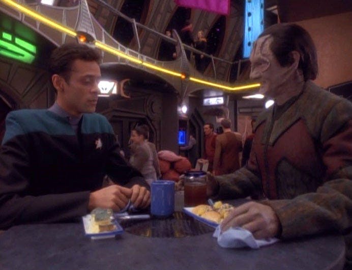 Julian Bashir and Garak engaged in conversation over a meal at the replimat in 'Distant Voices'