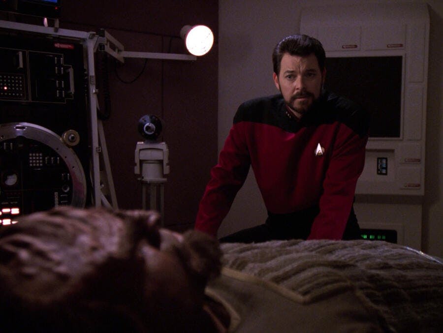 A concerned Riker leans over a paralyzed Worf in his med-bed in 'Ethics'