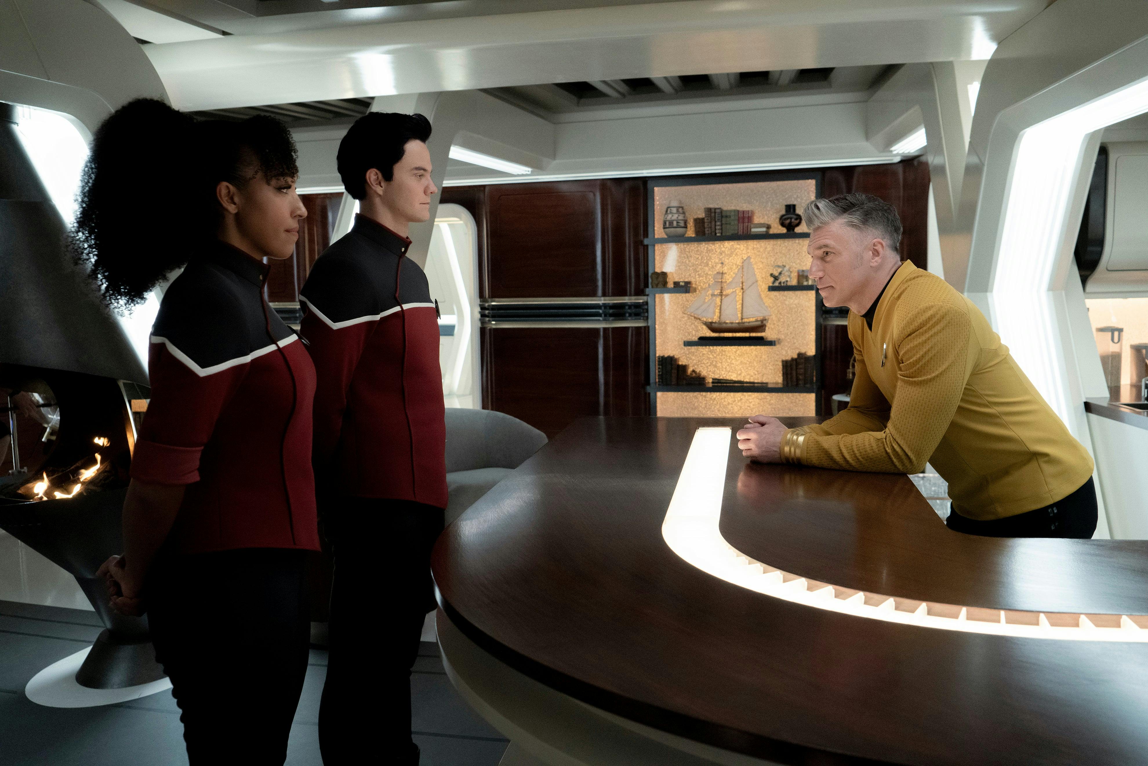 In his captain's quarters, Pike leans over his bar table and cautions Ensign Boimler and Mariner on the trouble they've caused in 'Those Old Scientists'