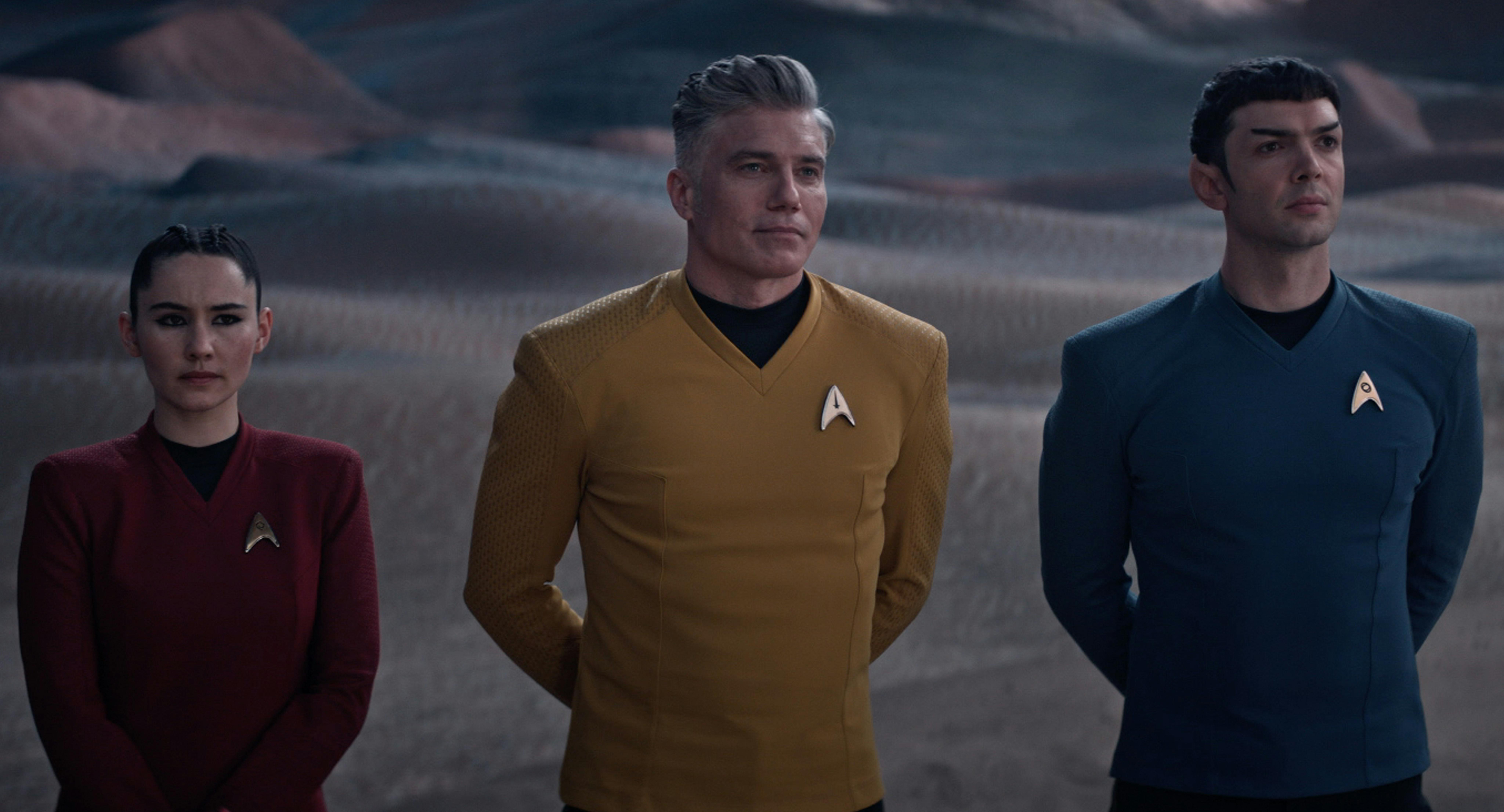Still of Star Trek: Strange New World's La'an, Captain Pike, and Spock standing with hands clasped behind them on a sandy, desert terrain 