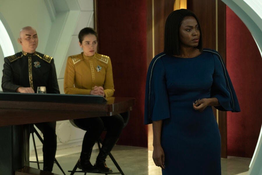 Counsellor Neera Ketoul stands and questions an off-screen witness while Pasalk and Batel sit at the table behind her in court in 'Ad Astra per Aspera'