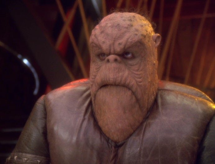 Morn sits in Quark's bar, silent as usual, in 'Who Mourns for Morn?'