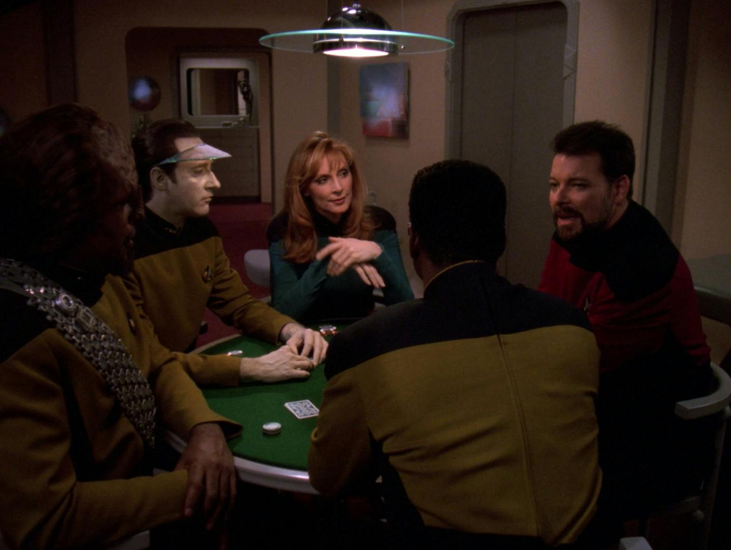 In crew quarters, sitting around a poker table, Worf, Data, Crusher, Riker, and La Forge weigh the information Picard revealed to them about the future in 'All Good Things...'