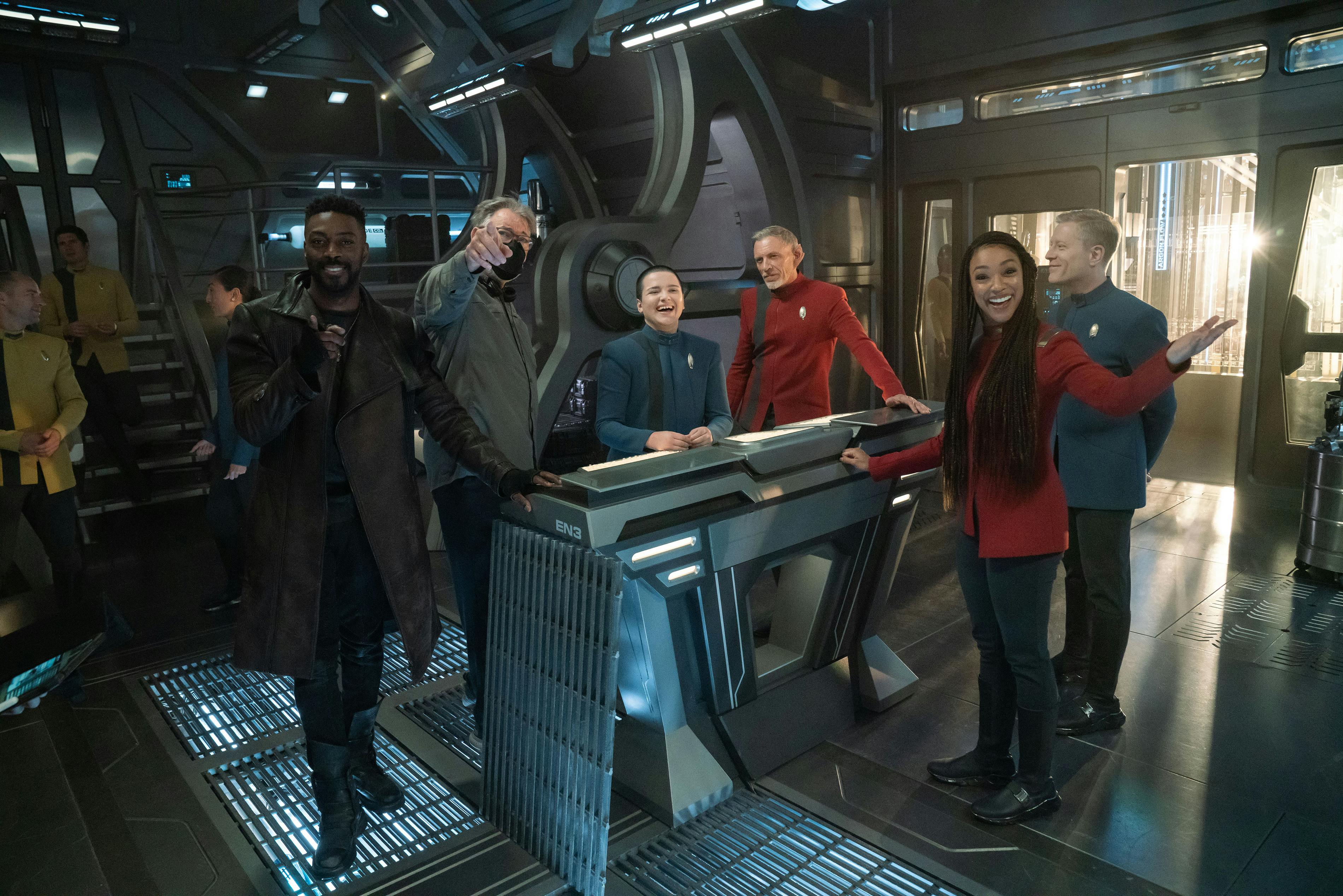 Behind-the-scenes of 'Lagrange Point' - David Ajala and Jonathan Frakes point ahead of them, Blu del Barrio laughs, Callum Keith Rennie poses, Sonequa Martin-Green smiles, while Paul Stamets smiles facing Frakes and del Barrio