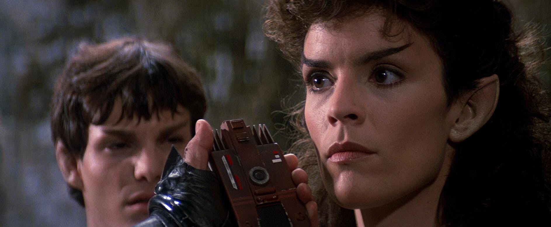 A close-up of Saavik's expression as a Klingon holds a communicator to her as a younger Spock looks towards her in Star Trek III: The Search for Spock