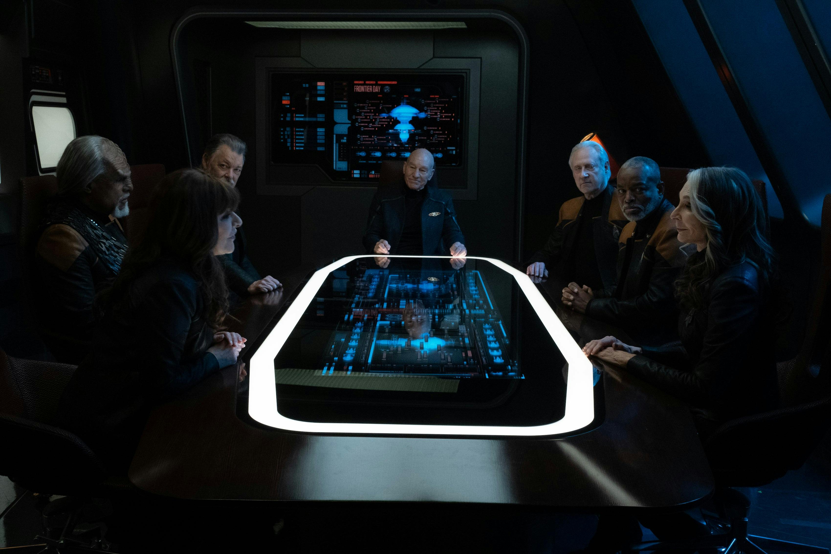 The Enterprise crew (Deanna Troi, Worf, Will Riker, Jean-Luc Picard, Data, Geordi La Forge, and Beverly Crusher) sit all together around the table in the Titan's Observation Lounge