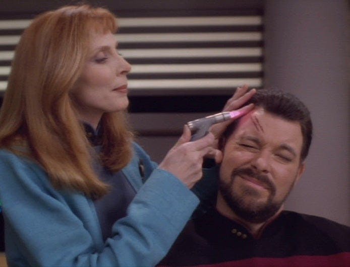 Crusher helps Riker with wound
