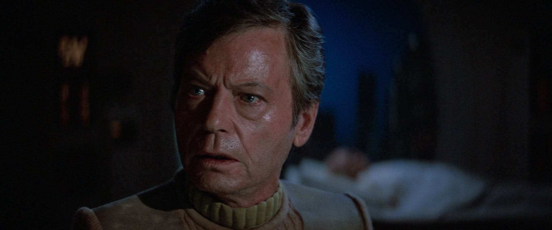 With a vision of his ailing father lying behind him, McCoy's face reflects immense grief that even with all his knowledge, he can't save his father in Star Trek V: The Final Frontier