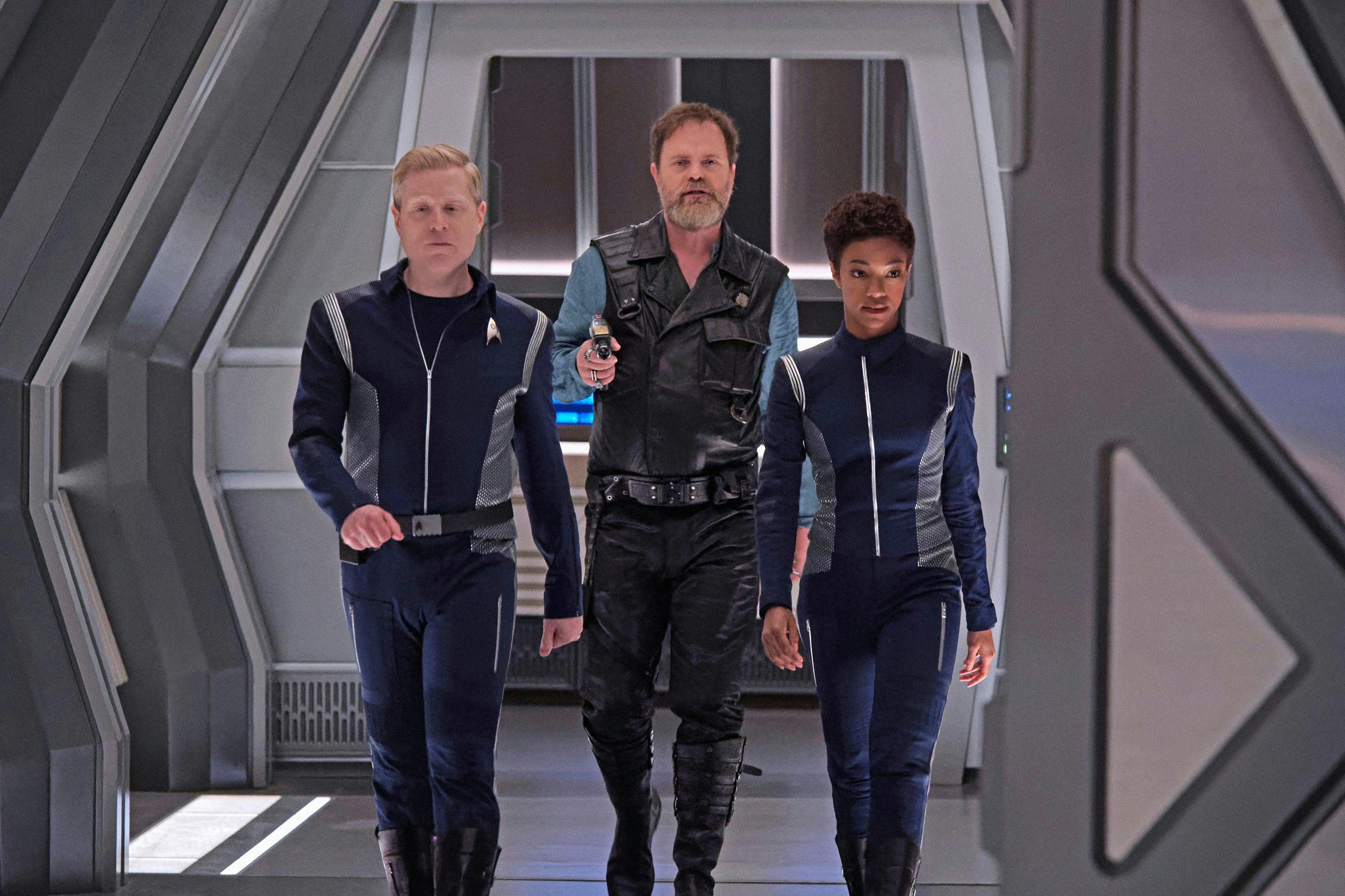 Harry Mudd forces Paul Stamets and Michael Burnham down the Discovery hallway as he trails behind them holding them at phaser gunpoint in 'Magic to Make the Sanest Man Go Mad'