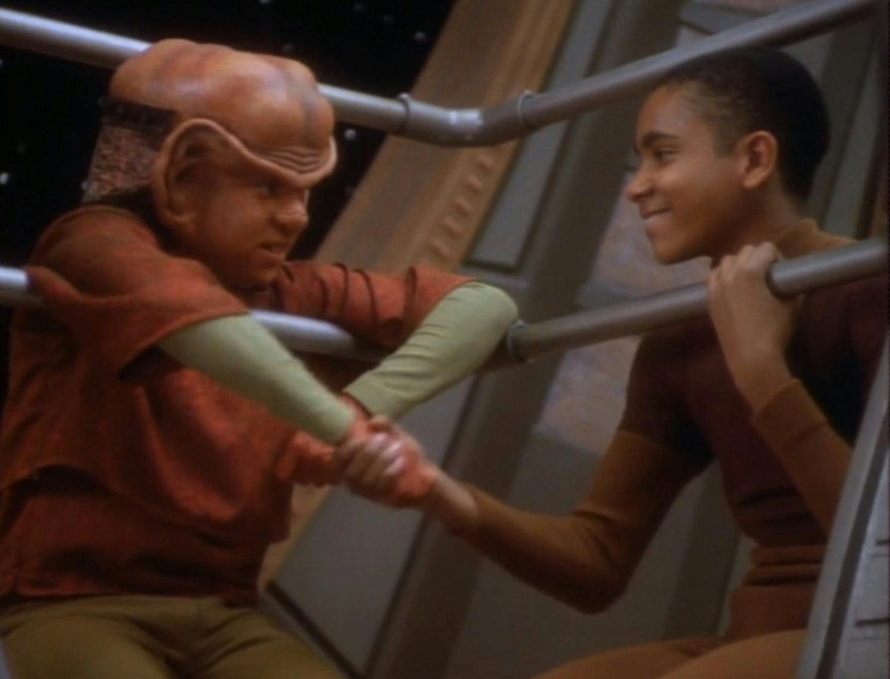 Leaning against the railings on the Promenade, Nog and Jake Sisko shake hands in 'The Nagus'