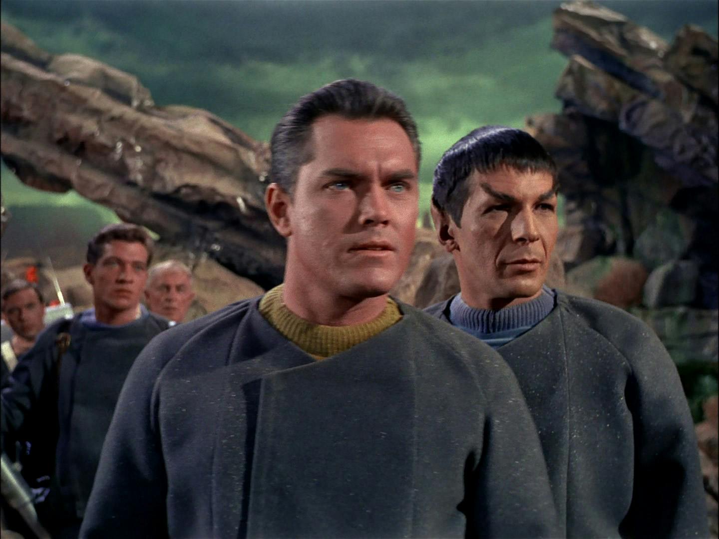 Captain Pike, Spock, and the rest of the landing party standing behind them on the surface of Talos IV as they face a group of scientists from the S.S. Columbia in 'The Cage'