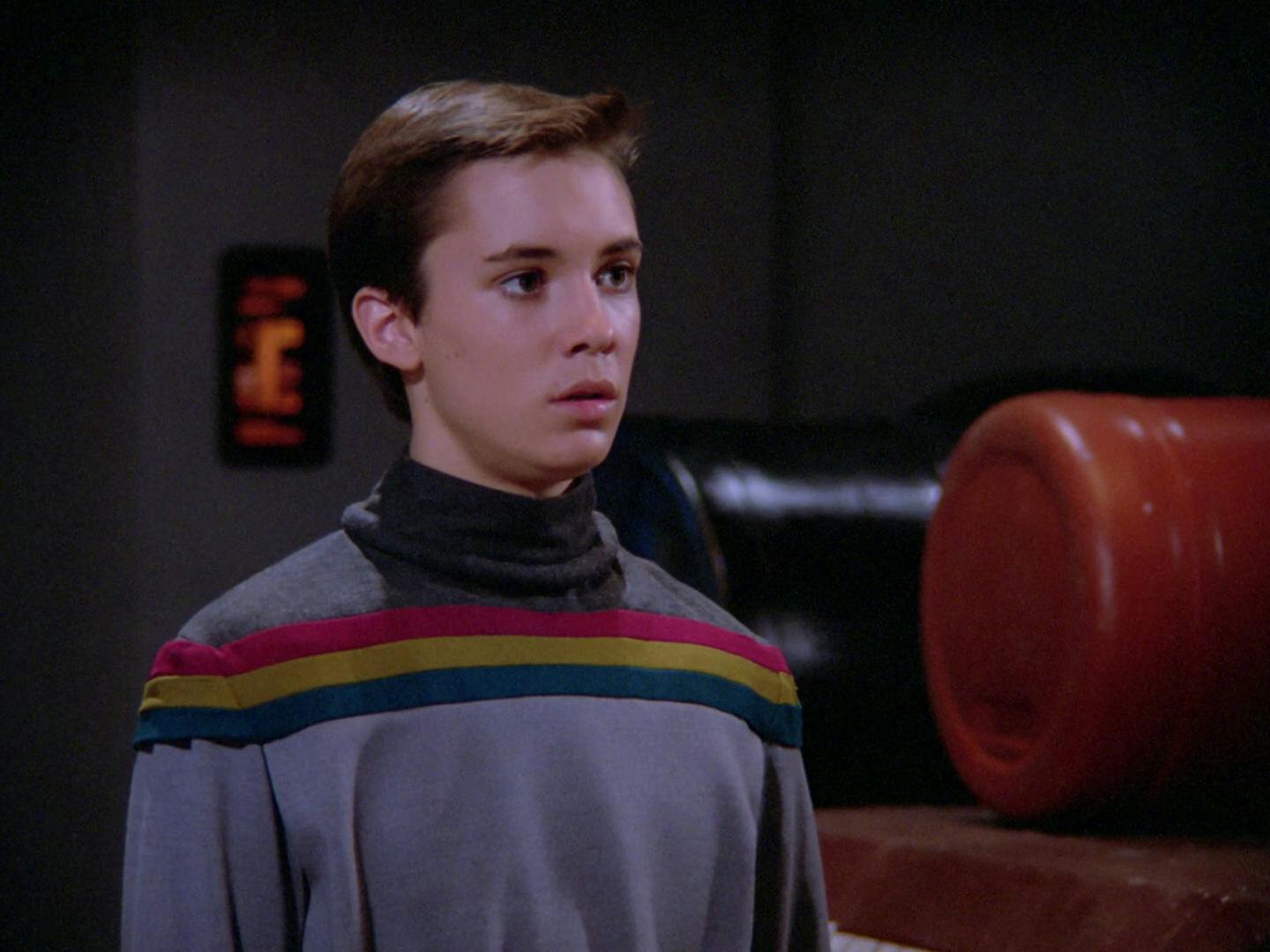 Wesley stands while wearing his rainbow striped grey sweater in 'Datalore'