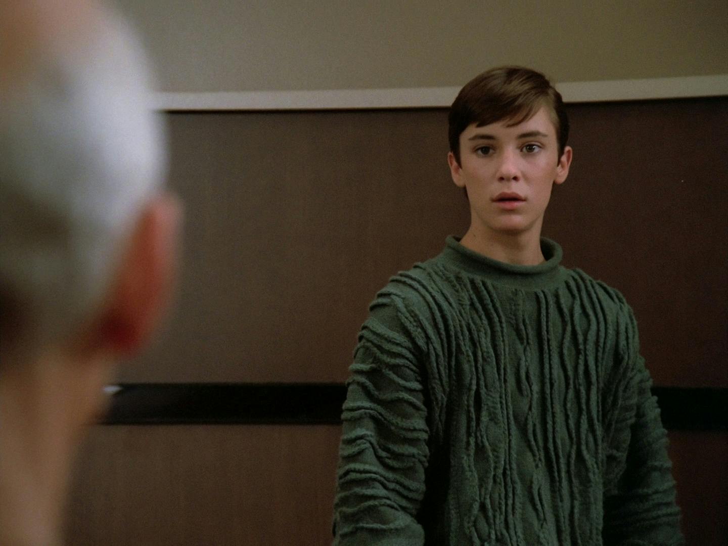 On the bridge of the Enterprise, Wesley Crusher wearing his thick knit green sweater looks directly at Picard in 'Encounter at Farpoint'