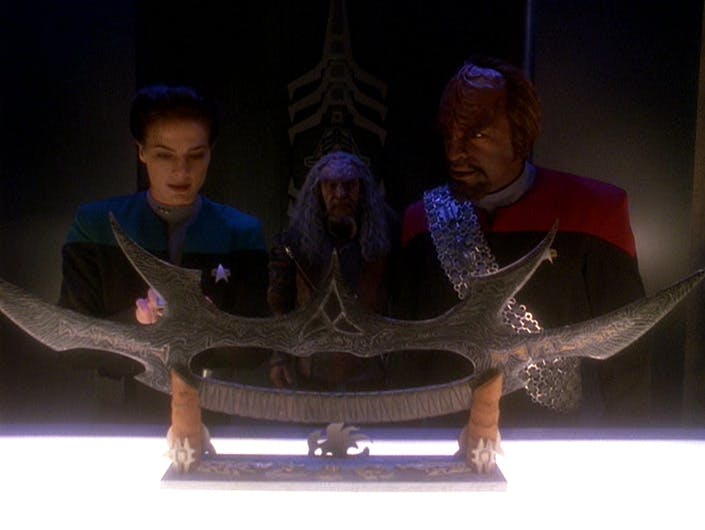 Jadzia Dax analyzes the readings on her tricorder as Worf and Kor are in shock over the presence of the Sword of Kahless