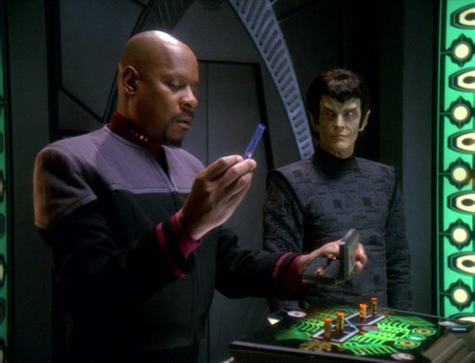 Sisko lifts a vial of bio-mimetic gel, manufacturing evidence for the Dominion War, as a Romulan observes him in 'In the Pale Moonlight'