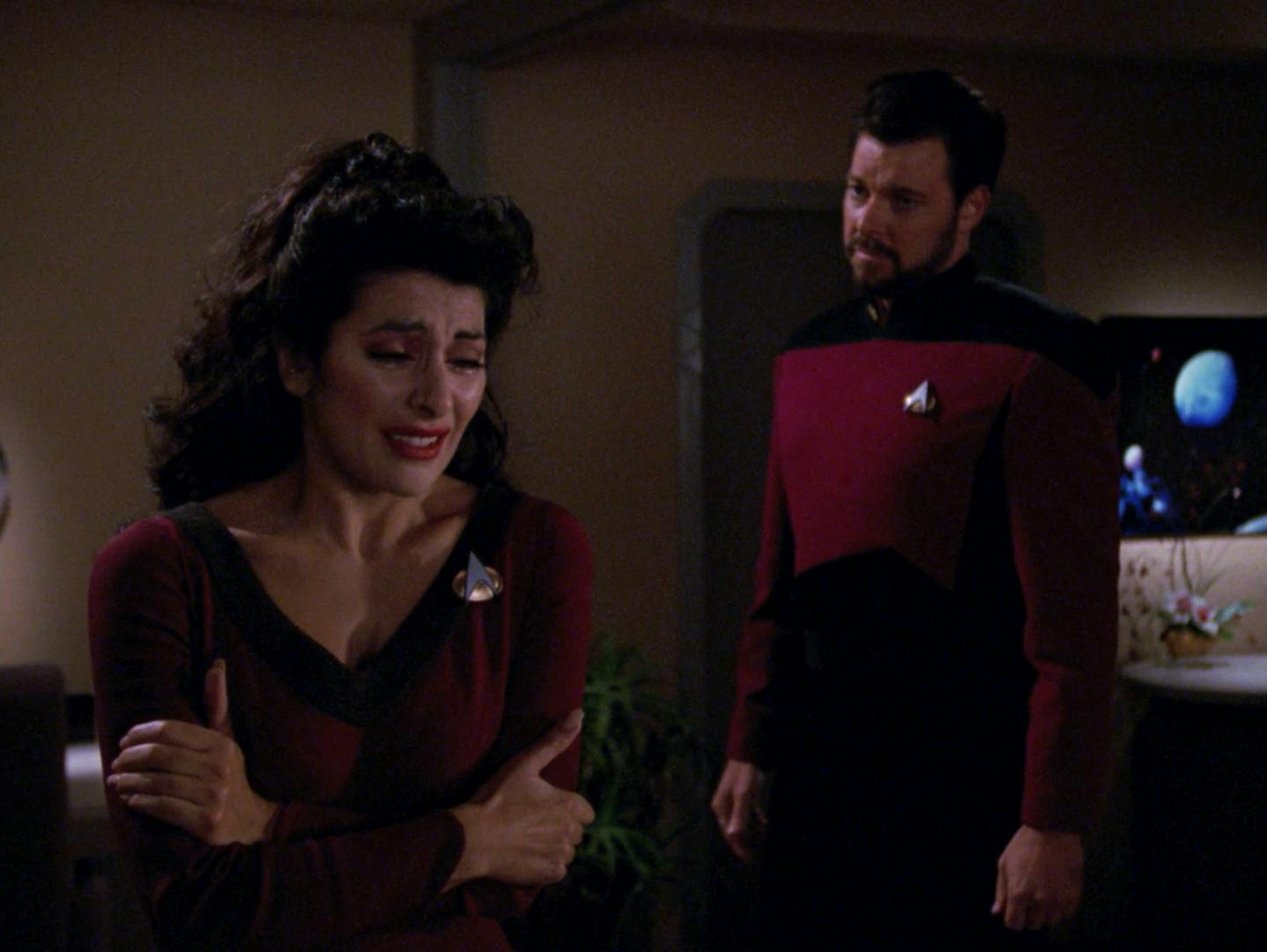 In her quarters, Deanna Troi embraces herself while crying over the loss of her abilities while Riker stands behind her concerned in 'The Loss'