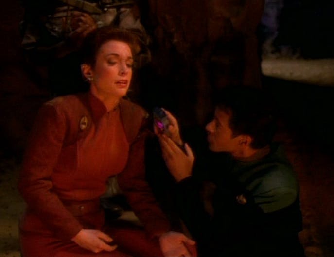 Julian Bashir crouches besides an injured Kira scanning her with his tricorder in 'Battle Lines'