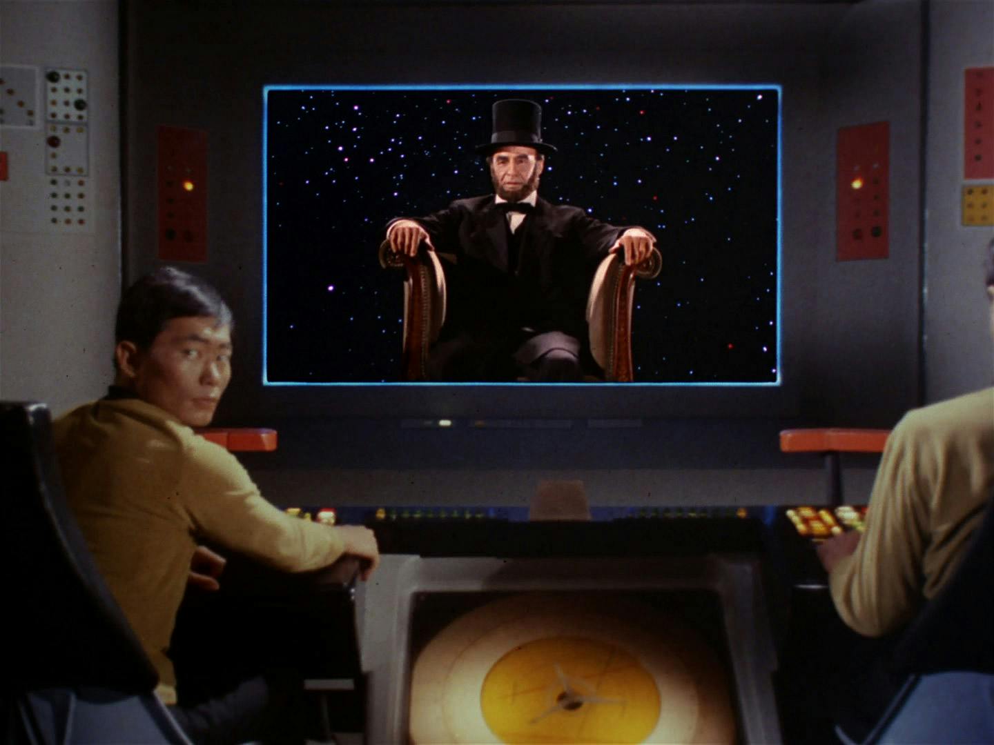 On the viewscreen of the U.S.S. Enterprise, a seated President Abraham Lincoln floats in space as Hikaru Sulu looks over his shoulder back at the Captain in 'The Savage Curtain'