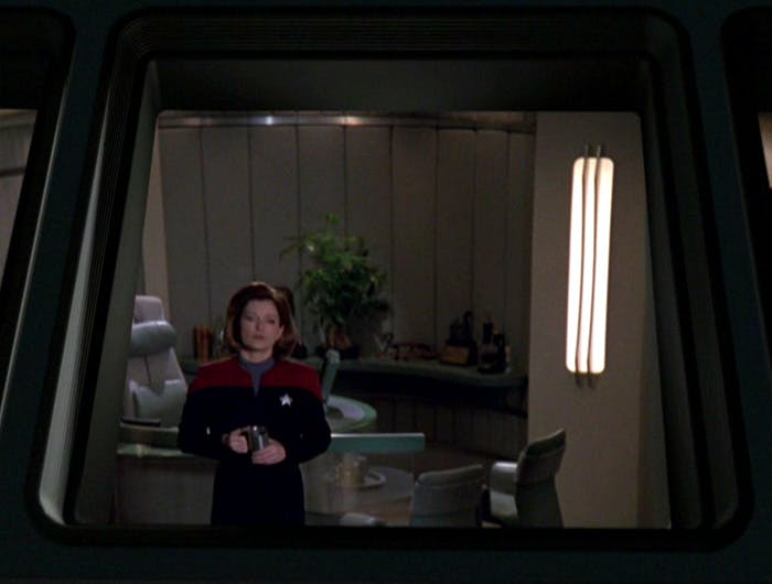 Captain Janeway holding a cup of coffee as she stands looking out the window of her ready room in 'Good Shepherd'