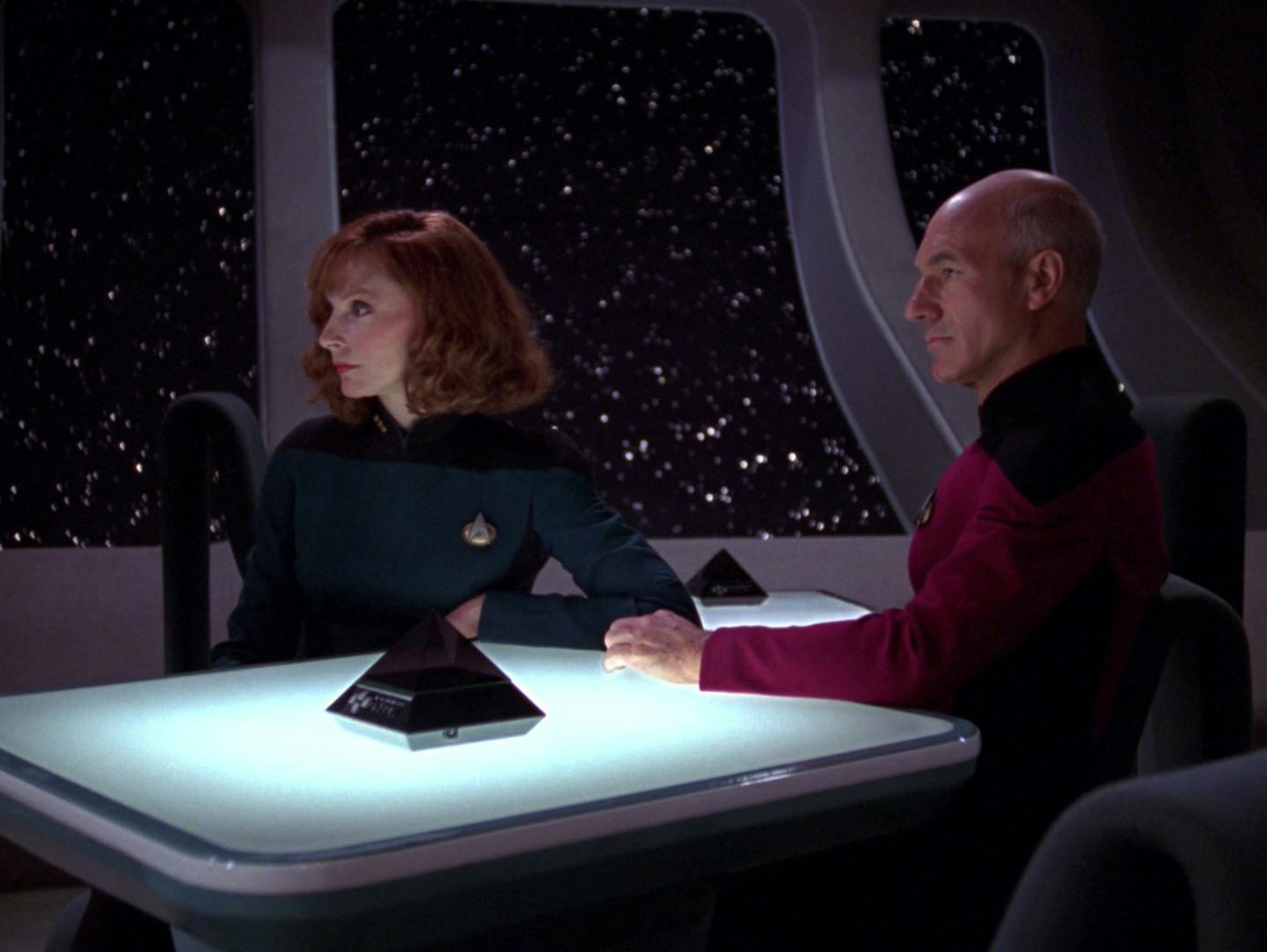 Beverly Crusher and Jean-Luc Picard are seated next to each other at a table in 10 Forward with the Pair Match console between them in 'The Ensigns of Command'