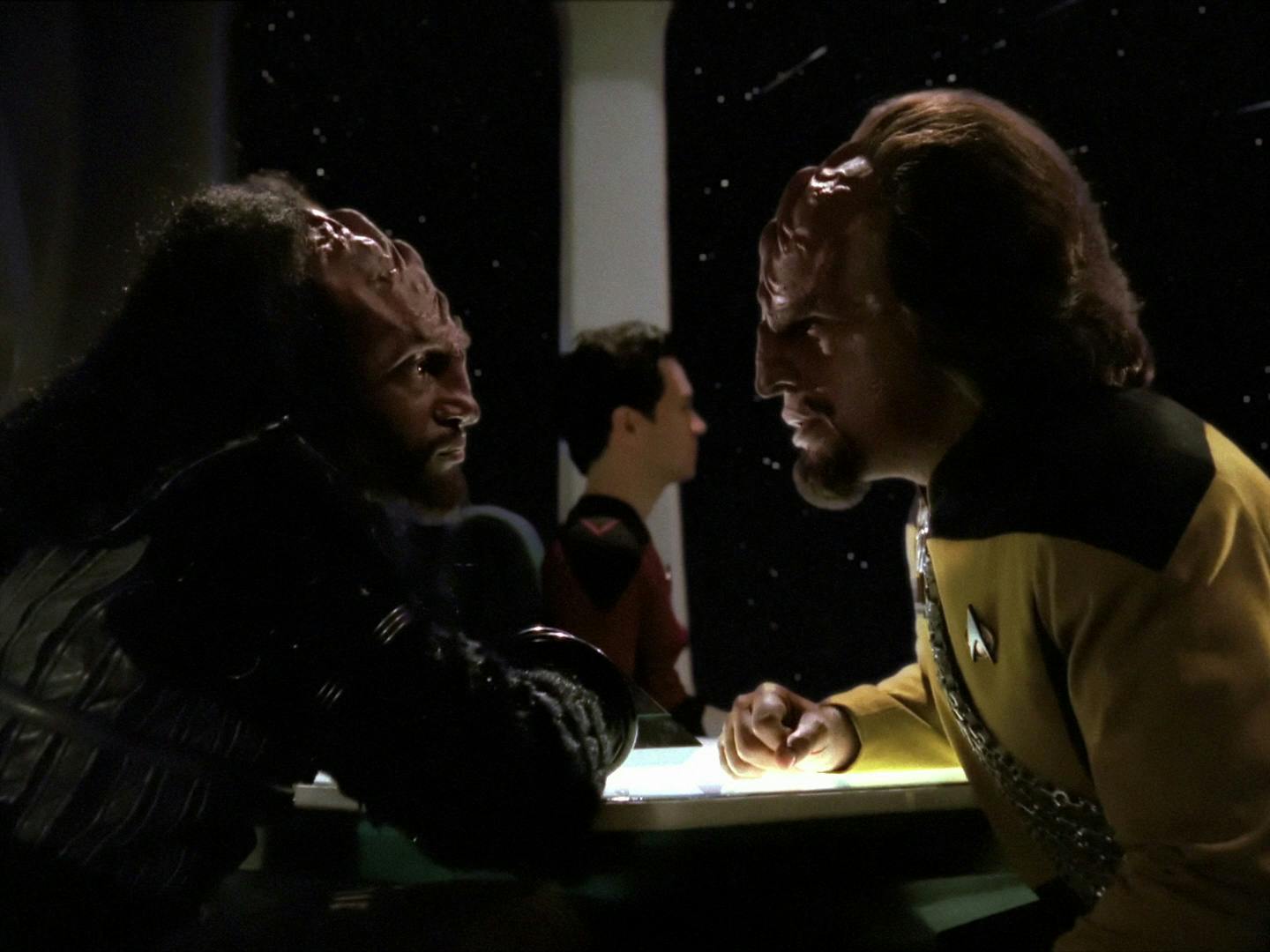 Kurn and Worf both lean in at a table at 10 Forward as they look directly at one another in 'Sins of the Father'