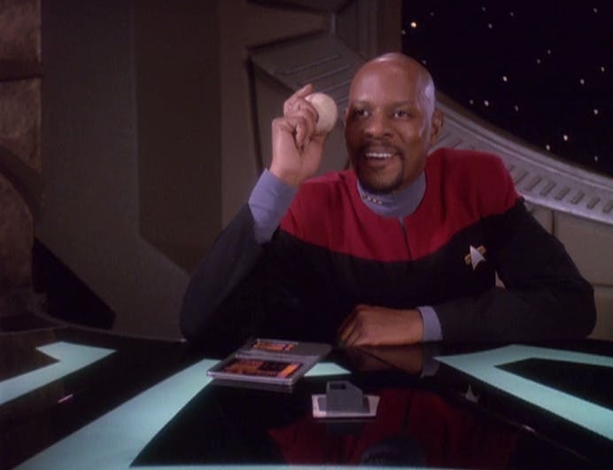 Captain Benjamin Sisko holds his beloved baseball in his hand with elbow on the table as he asks Kira if she'd like to go to a baseball game in 'Starship Down'