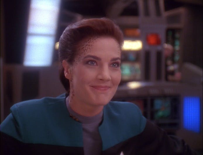 Jadzia Dax grins while standing at her station in 'Trials and Tribble-ations'