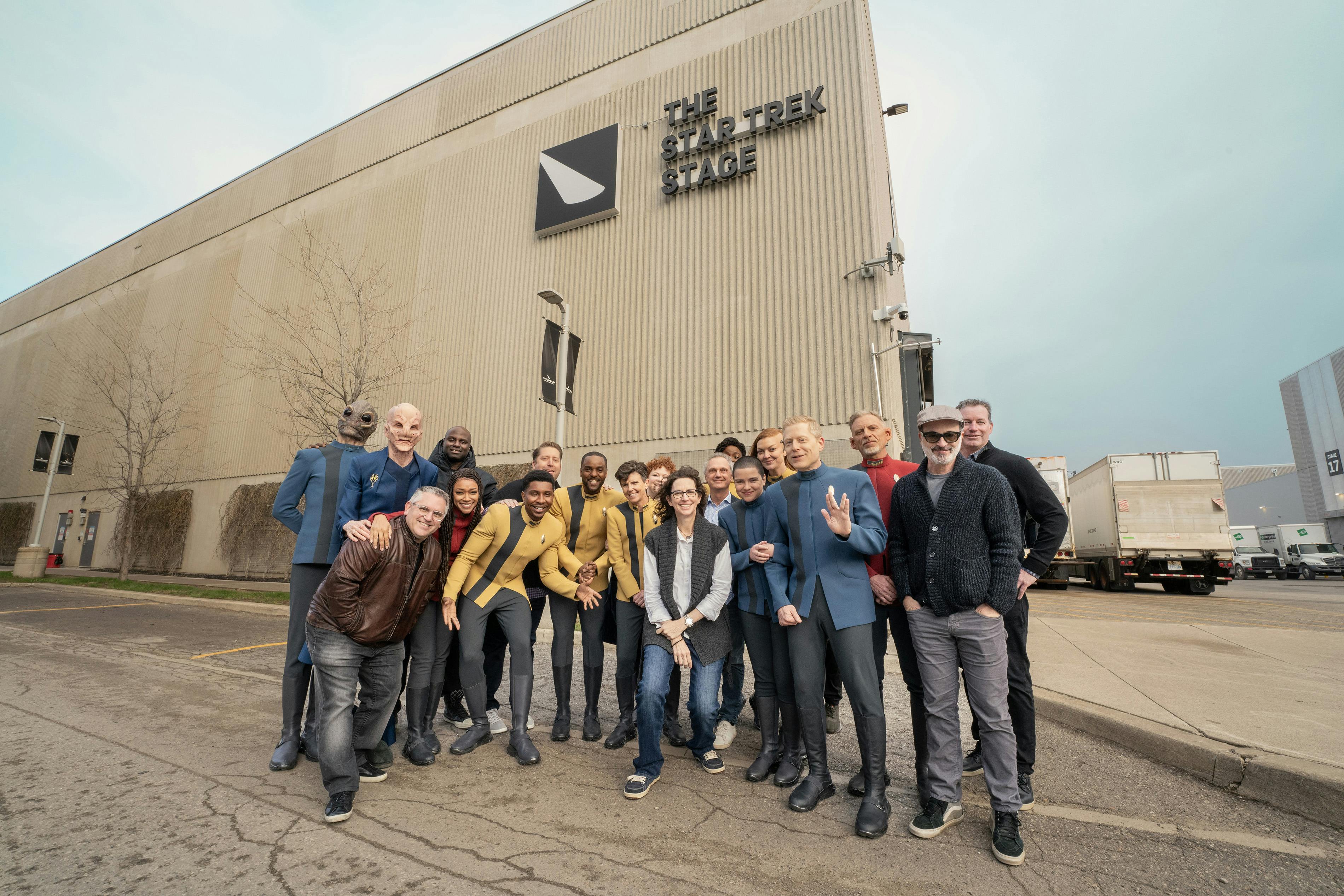 Cast and crew of Star Trek: Discovery in costume including Alex Kurtzman and Michelle Paradise stand in front of the newly renamed Star Trek stage in Pinewood Toronto