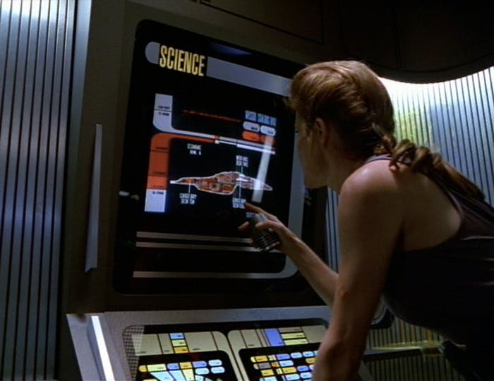 Captain Janeway, out of proper uniform and showcasing her biceps with a tank top, pulls up Voyager's schematics on the computer in 'Macrocosm'