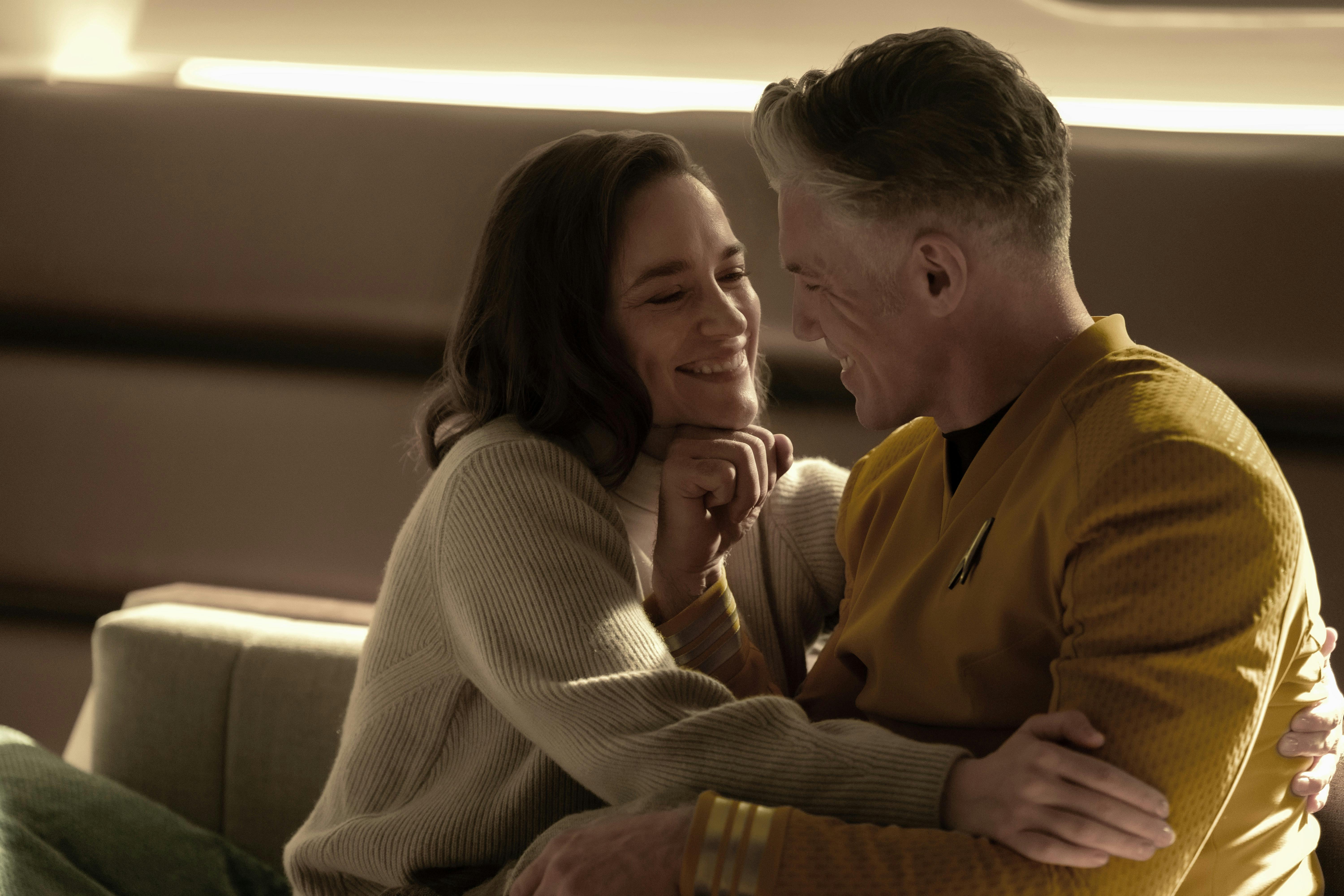 A smiling Captain Batel embraces Captain Pike on the couch in captain's quarters in 'Wedding Bell Blues'