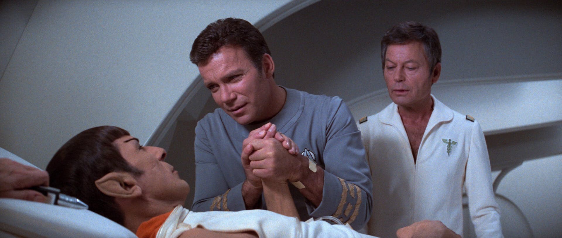 As Spock lays down in a med-bed, Kirk and McCoy stand at his bedside as Kirk grips Spock's hands in Star Trek: The Motion Picture