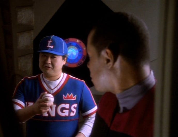 Benjamin Sisko looks over his shoulder behind him towards Buck Bokai in his Kings baseball uniform who lifts his hand with a baseball in it and points at Sisko in Star Trek: Deep Space Nine's 'If Wishes Were Horses'
