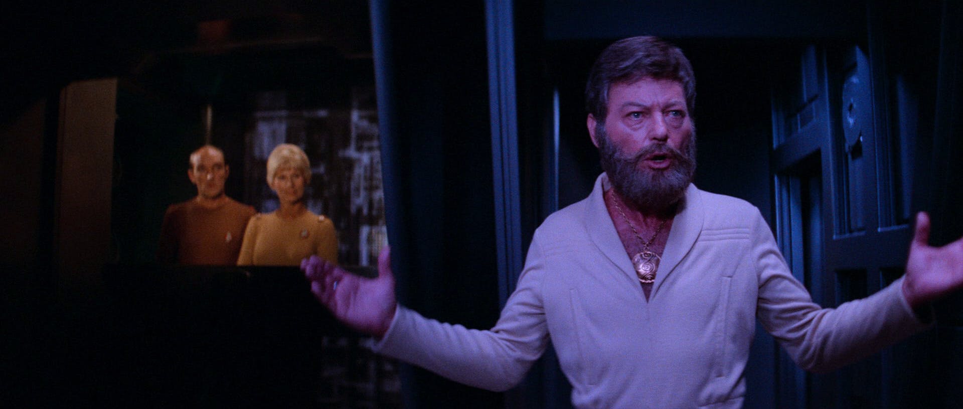 A bearded Leonard Bones McCoy, sporting a gold medallion, lifts his arms up in Star Trek: The Motion Picture