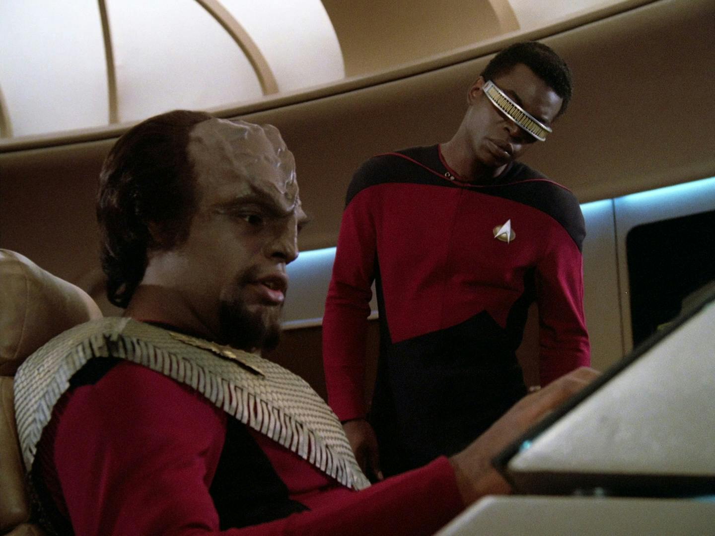 Worf sits at his station on the bridge of the Enterprise as Geordi La Forge looks over his shoulder at his control panel in 'Encounter at Farpoint'