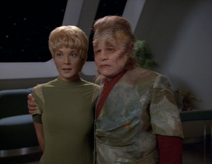 Standing in front of Captain Janeway, Kes and Neelix stand side-by-side as he wraps his arm around her shoulders in 'Caretaker'