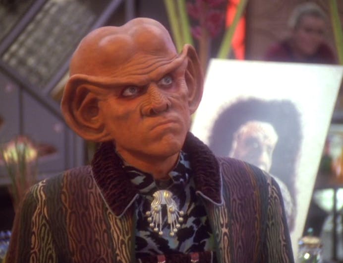 At his bar, Quark stands in front of a tribute of patron Morn during the memorial party at his bar in 'Who Mourns for Morn?'